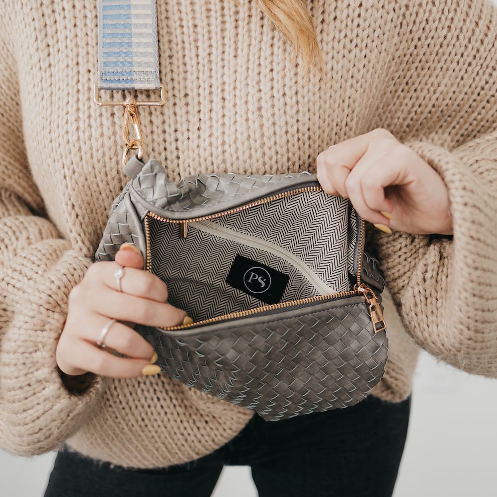 Person holding a gray woven handbag with a visible brand logo, wearing a beige sweater.